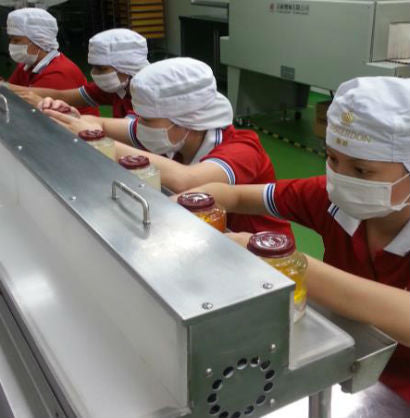 Workers in red uniforms, caps and masks capping jars of bird's nest on the Masterdon production line.